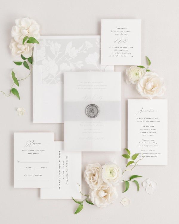 Alyssa wedding invitations flat lay with soft gray magnolia liner, soft gray belly band, translucent vellum jacket, and silver posy wax seal.