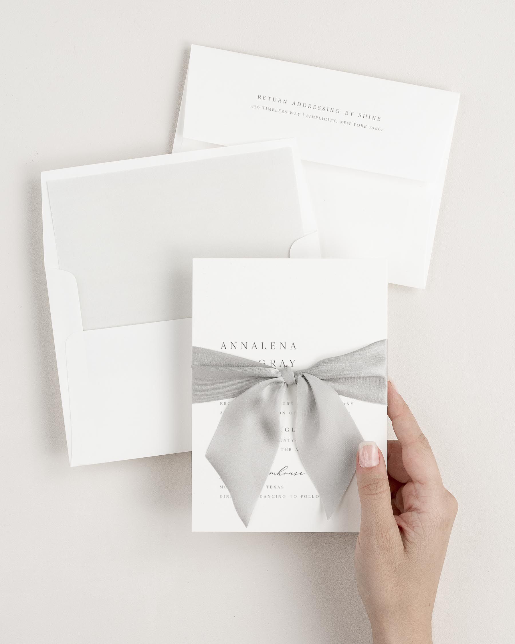 Bride holding Annalena wedding invitation tied with fog ribbon.