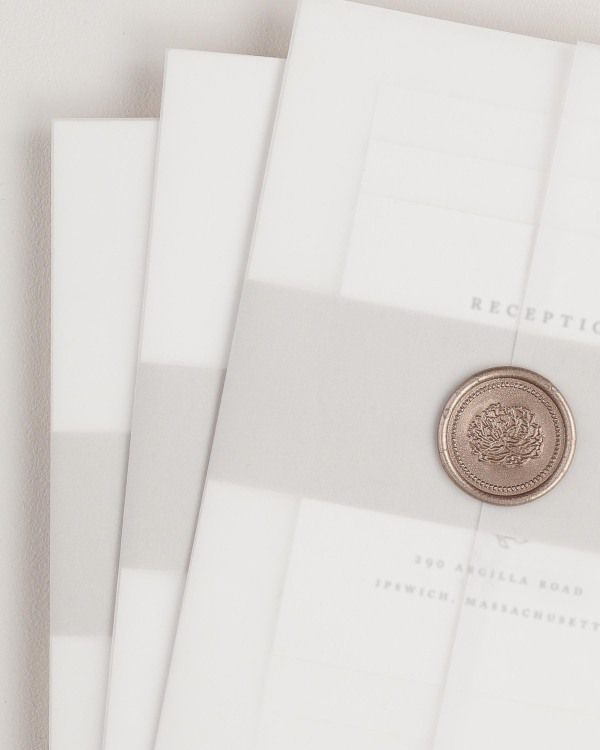 Aurora wedding invitation with a stone belly band, translucent vellum jacket, and bronze florette wax seal.