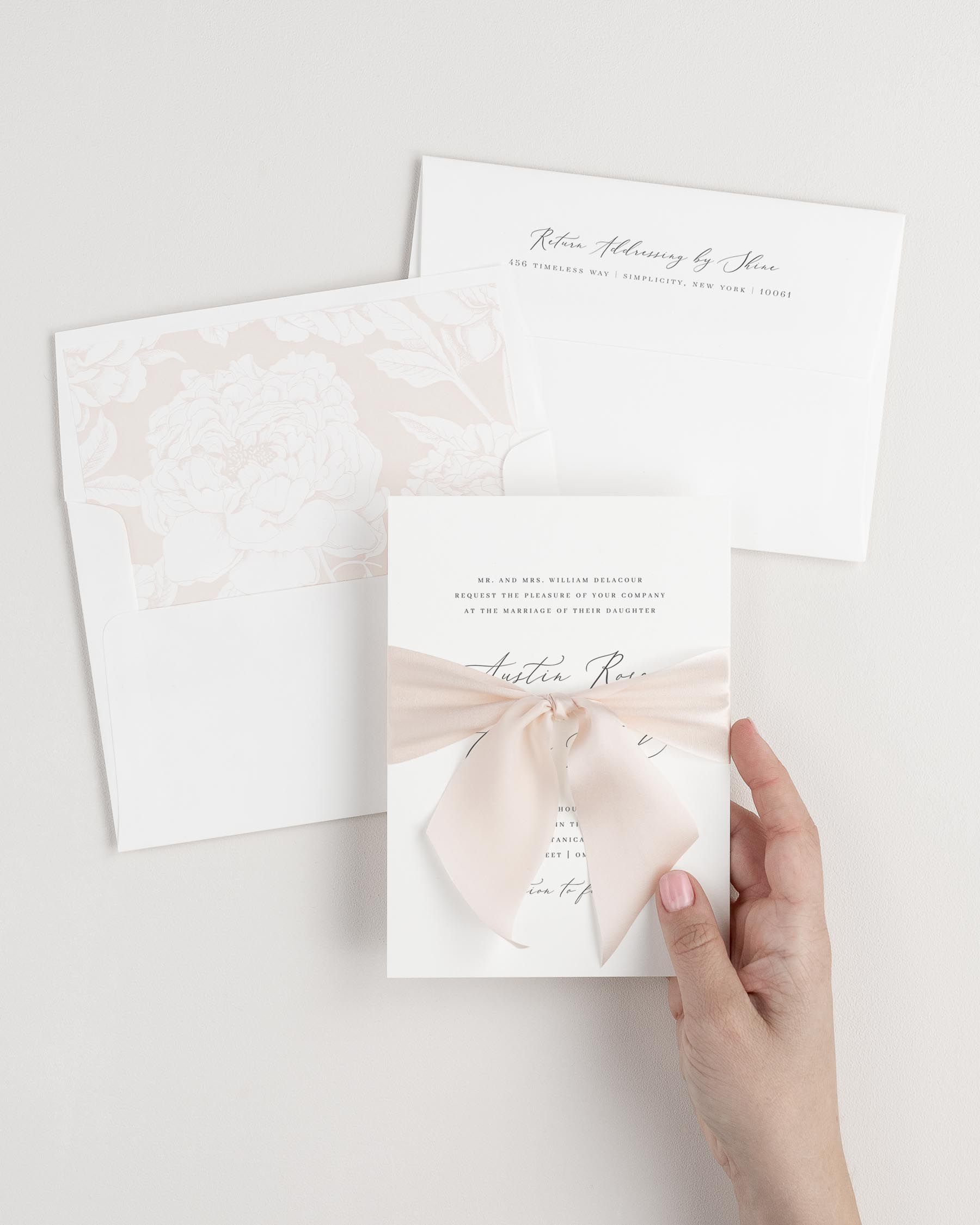 Bride holding Austin wedding invitation tied with pale pink ribbon.