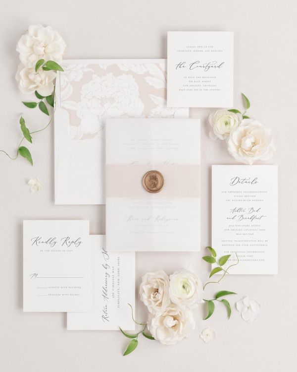 Cecilia wedding invitations flat lay with rose gold blooms liner, rose gold belly band, translucent vellum jacket, and gold posy wax seal.