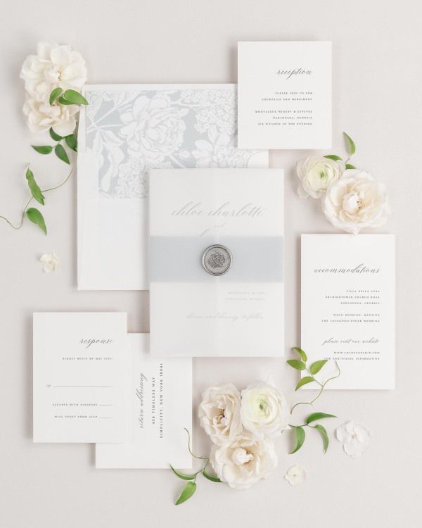 Chloe wedding invitations flat lay with cloud hydrangea liner, cloud belly band, translucent vellum jacket, and silver florette wax seal.