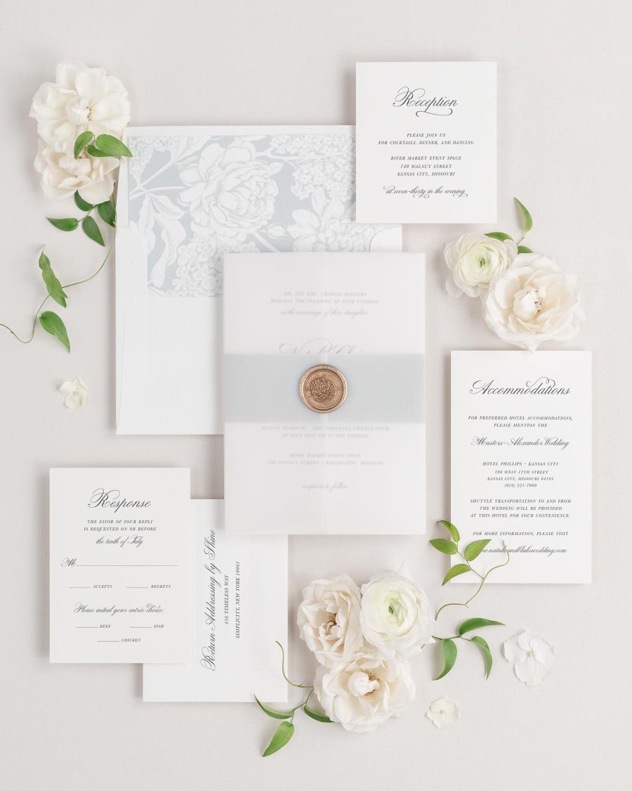 Classic Script wedding invitations flat lay with cloud hydrangea liner, cloud belly band, translucent vellum jacket, and gold florette wax seal.
