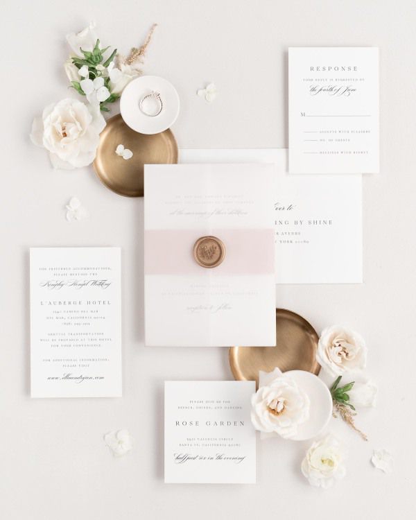 Ella wedding invitations flat lay with rose gold belly band, translucent vellum jacket, and gold posy wax seal.