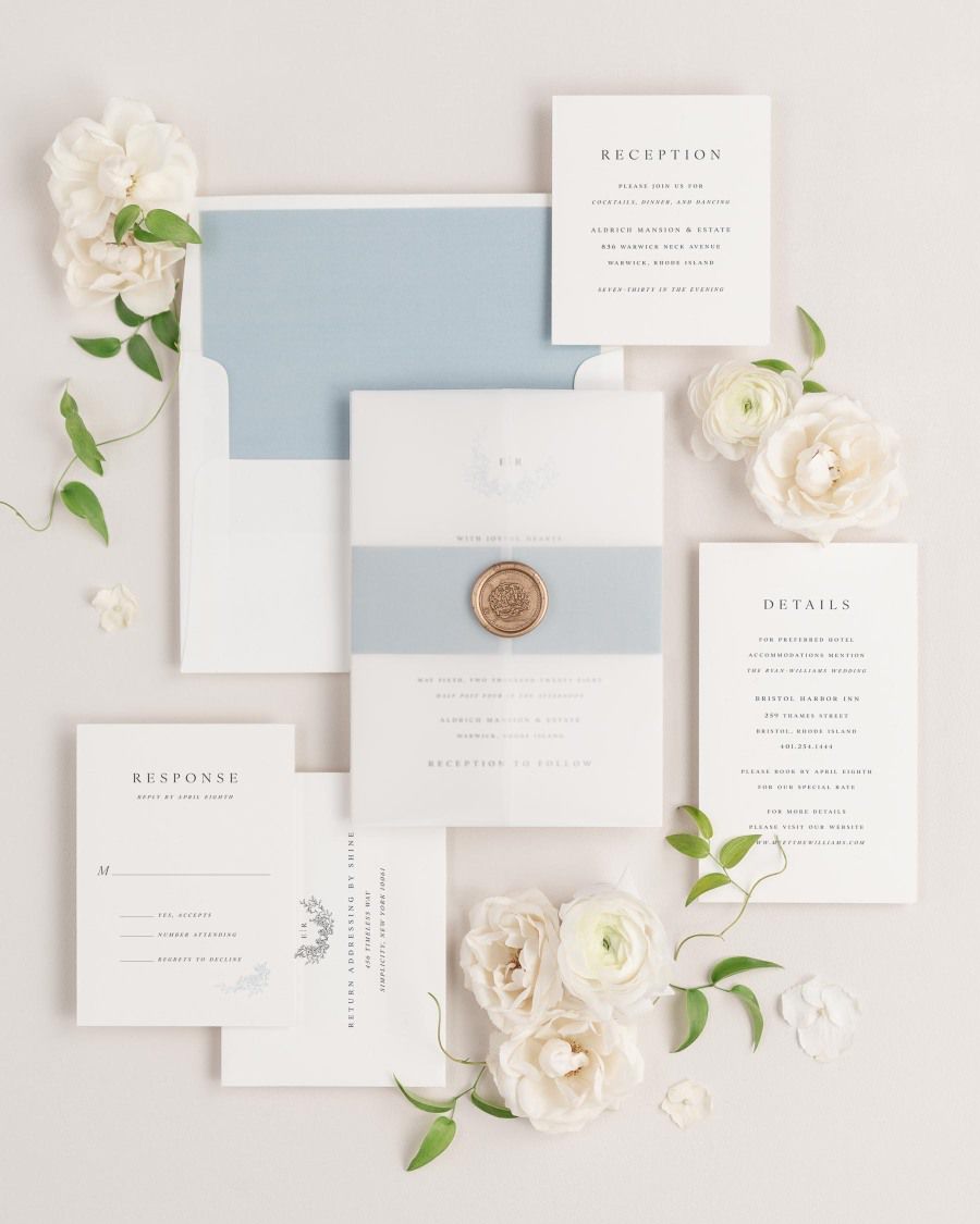 Emily wedding invitation with a dusty blue belly band, translucent vellum jacket, and gold florette wax seal.