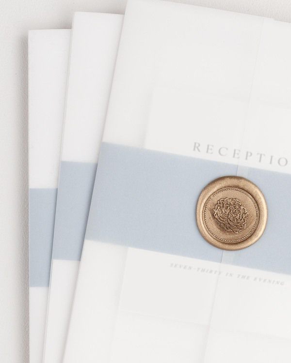 Emily wedding invitation with a dusty blue belly band, translucent vellum jacket, and gold florette wax seal.