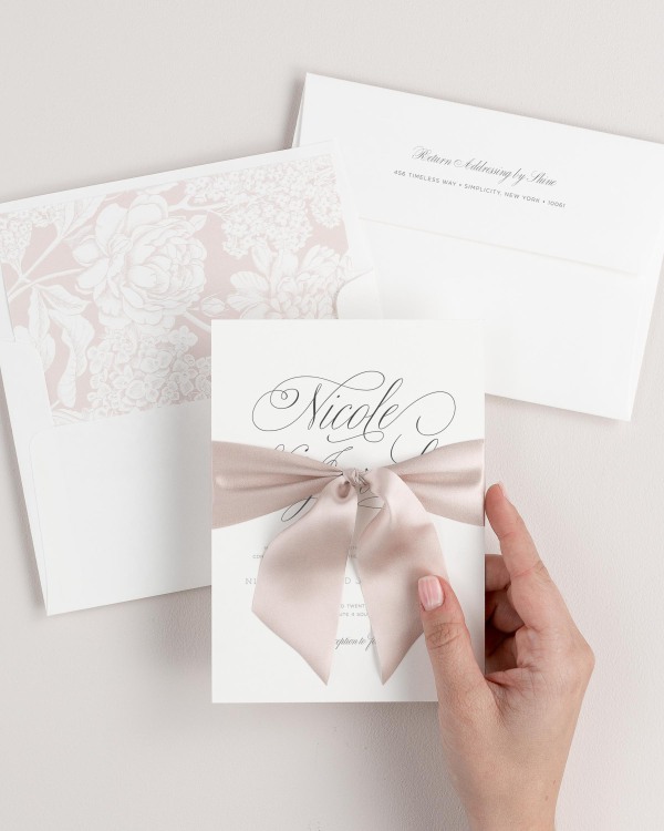 Bride holding Garden Script wedding invitation tied with antoinette ribbon.