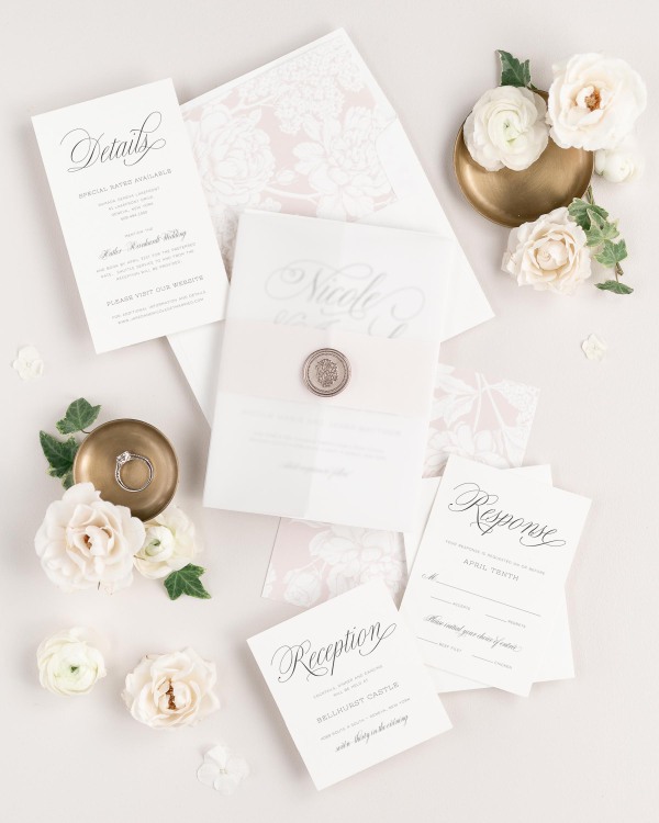 Garden Script wedding invitations flat lay with vintage blush hydrangea liner, vintage blush belly band, translucent vellum jacket, and bronze florette wax seal.