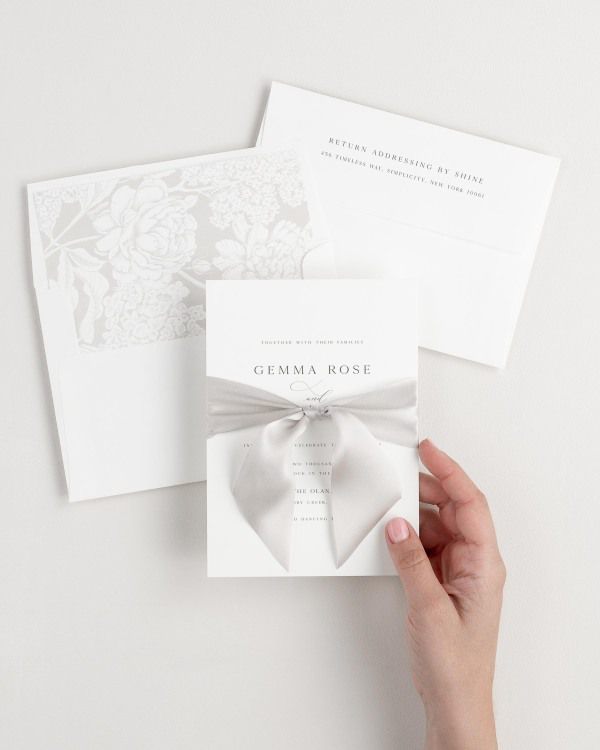 Bride holding Gemma wedding invitation tied with mink ribbon.