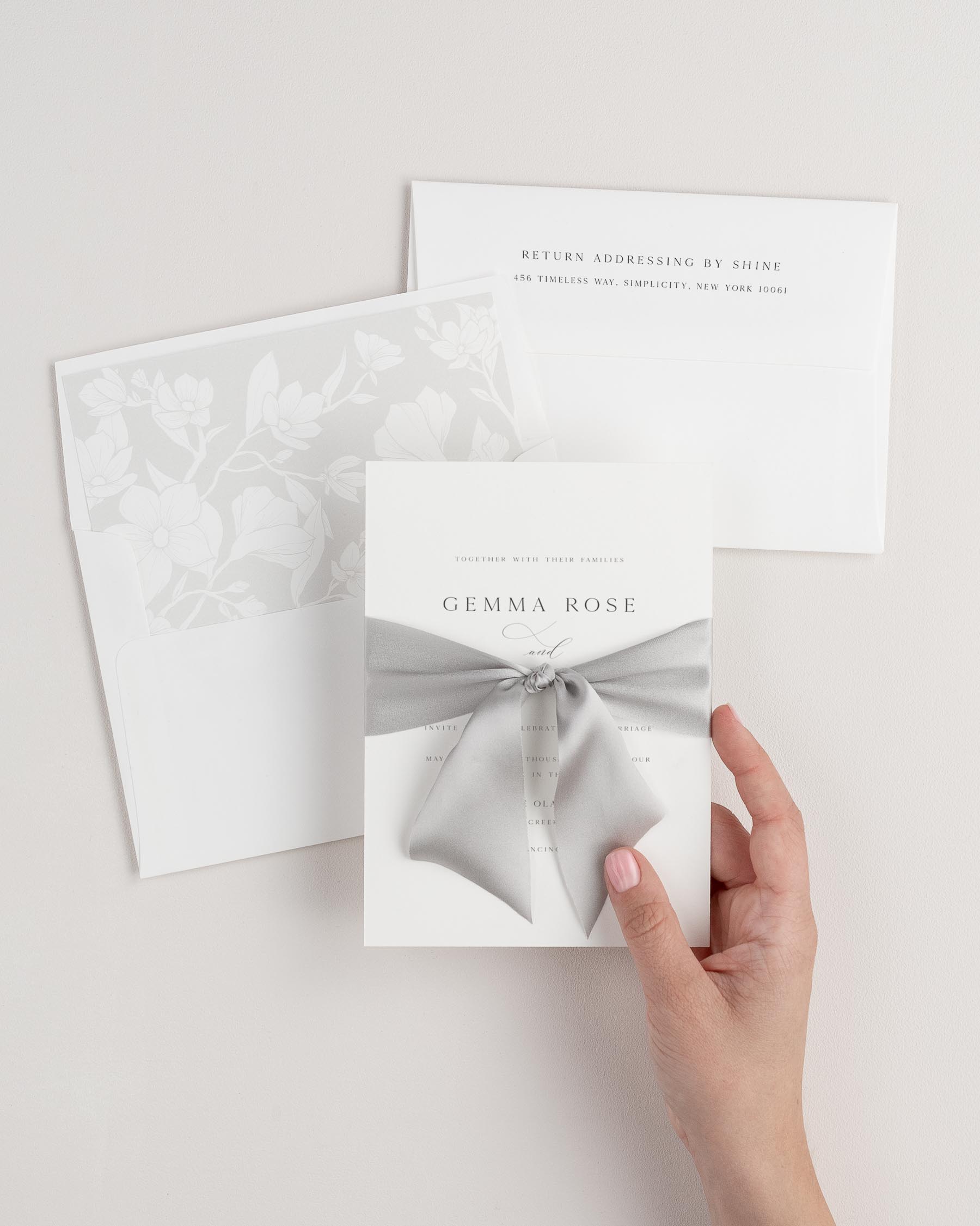 Bride holding Gemma wedding invitation tied with fog ribbon.