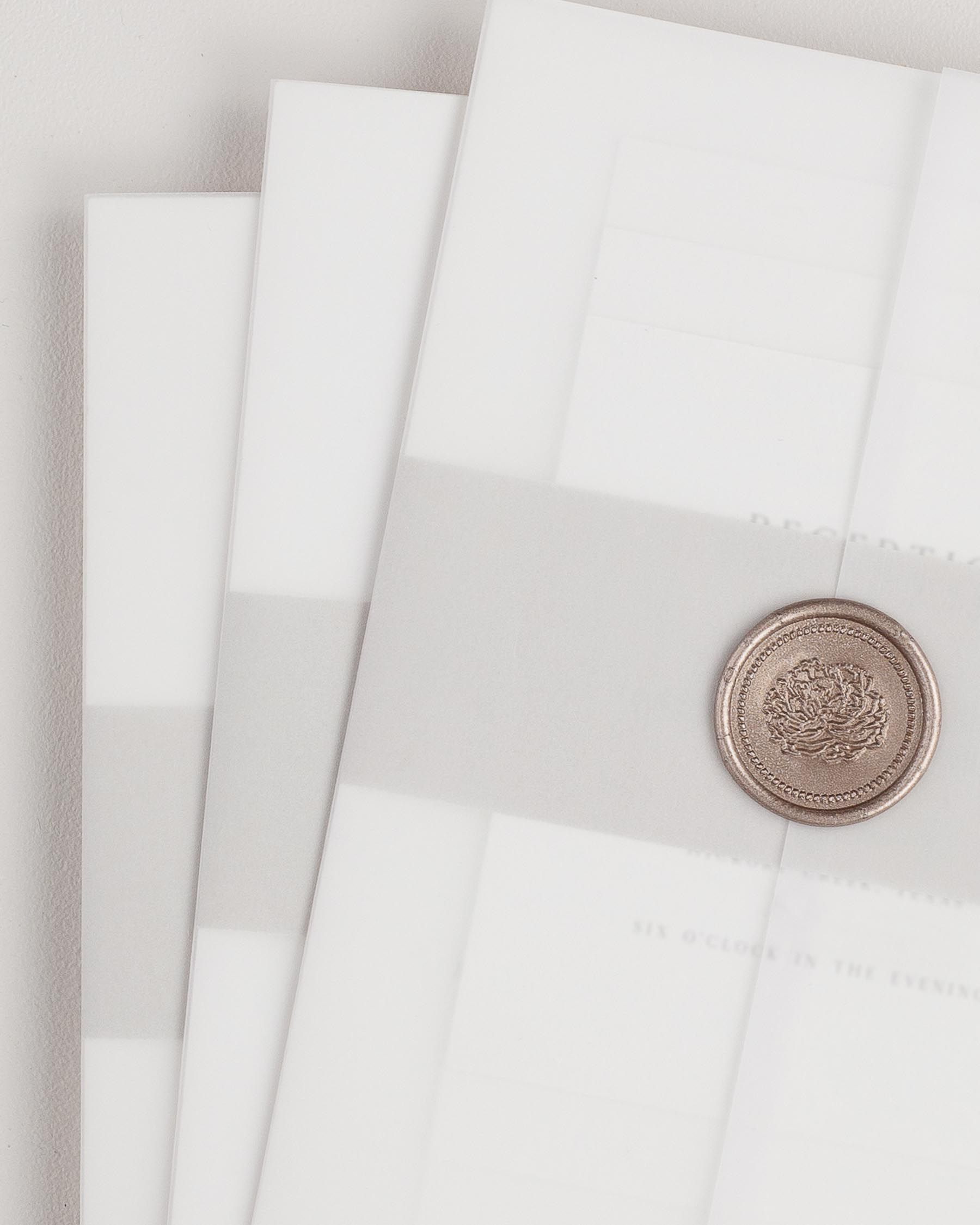 Gemma wedding invitation with a stone belly band, translucent vellum jacket, and bronze florette wax seal.