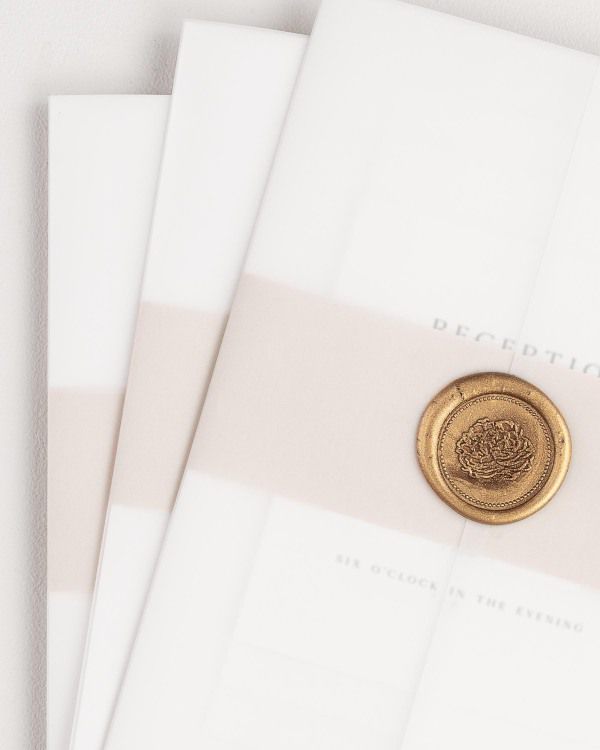 Gemma wedding invitation with a rose gold belly band, translucent vellum jacket, and gold florette wax seal.