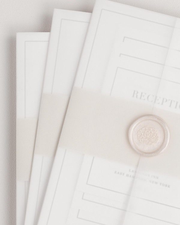 Glam Monogram wedding invitation with a nude belly band, translucent vellum jacket, and bronze florette wax seal.