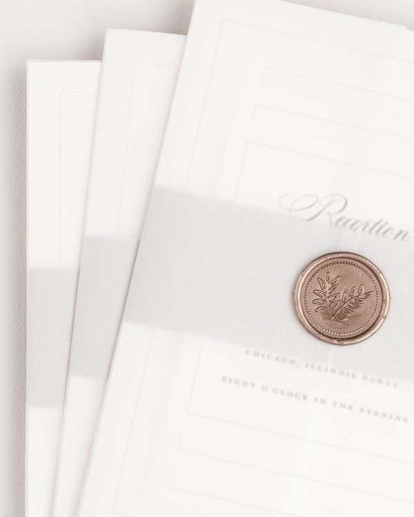 Grace wedding invitation with a soft gray belly band, translucent vellum jacket, and gold wreath wax seal.