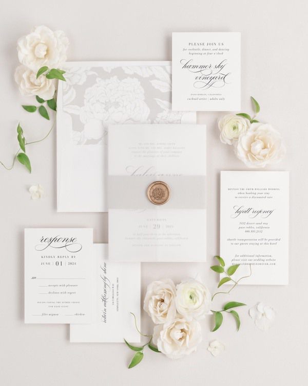 Haley wedding invitations flat lay with stone blooms liner, stone belly band, translucent vellum jacket, and gold florette wax seal.