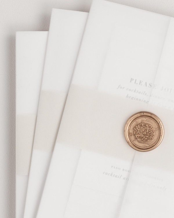 Haley wedding invitation with a nude belly band, translucent vellum jacket, and gold florette wax seal.