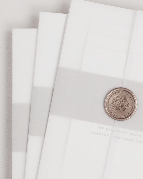 Jessica wedding invitation with a stone belly band, translucent vellum jacket, and bronze florette wax seal.