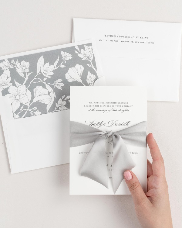 Bride holding Kaitlyn wedding invitation tied with fog ribbon.