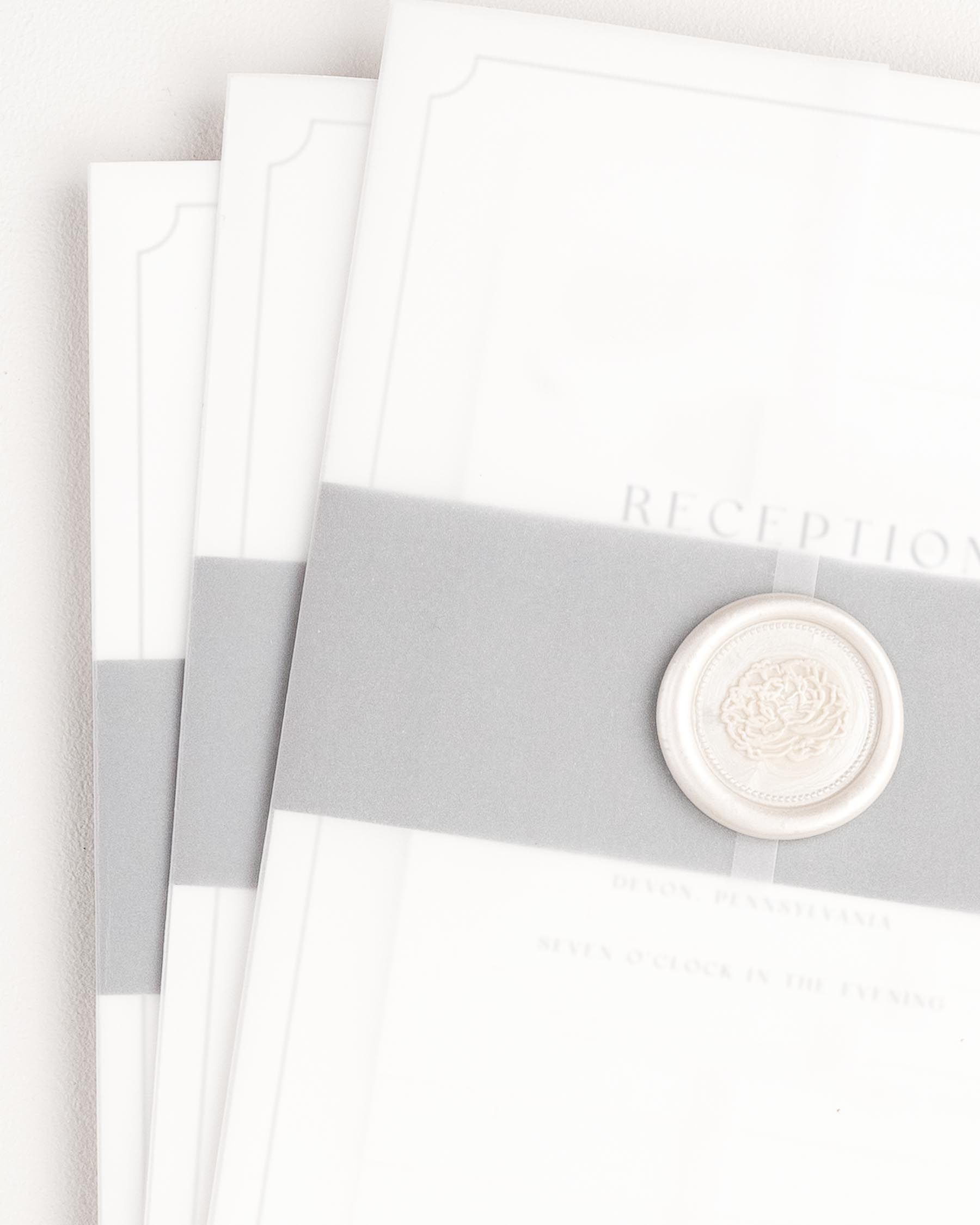 Kendall wedding invitation with a slate belly band, translucent vellum jacket, and pearl florette wax seal.