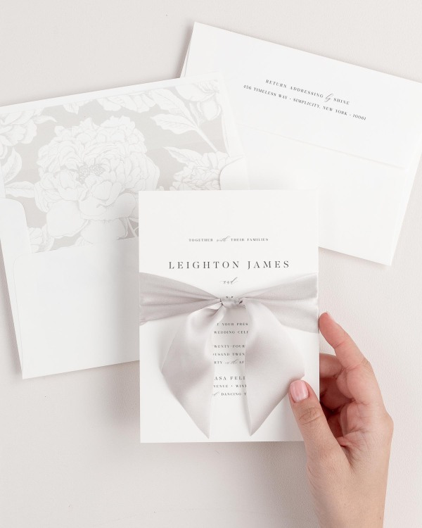 Bride holding Leighton wedding invitation tied with mink ribbon.