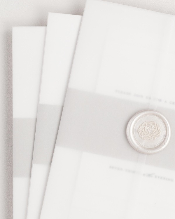 Leighton wedding invitation with a feather belly band, translucent vellum jacket, and pearl florette wax seal.