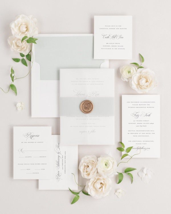 Liliana wedding invitations flat lay with sea salt solid liner, sea salt belly band, translucent vellum jacket, and gold wreath wax seal.
