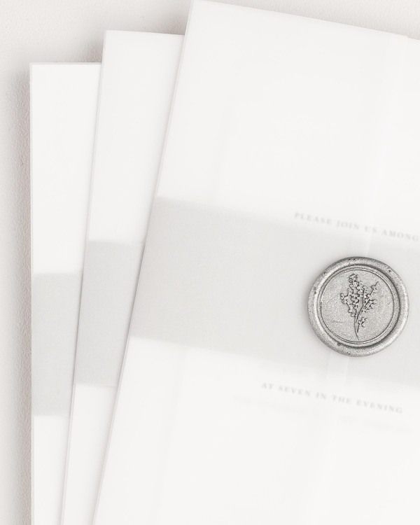 Lucille wedding invitation with a soft gray belly band, translucent vellum jacket, and silver posy wax seal.