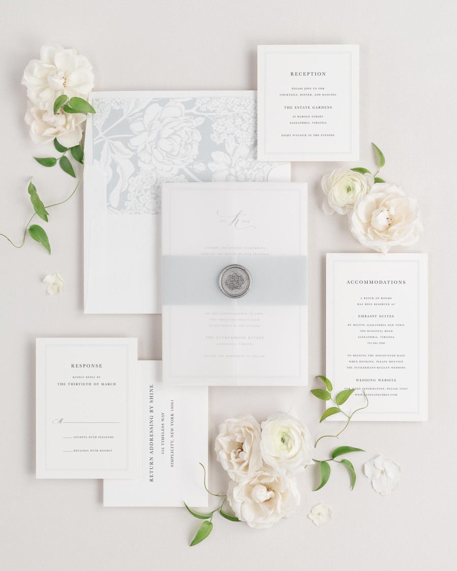 Mackenzie wedding invitations flat lay with cloud hydrangea liner, cloud belly band, translucent vellum jacket, and silver florette wax seal.