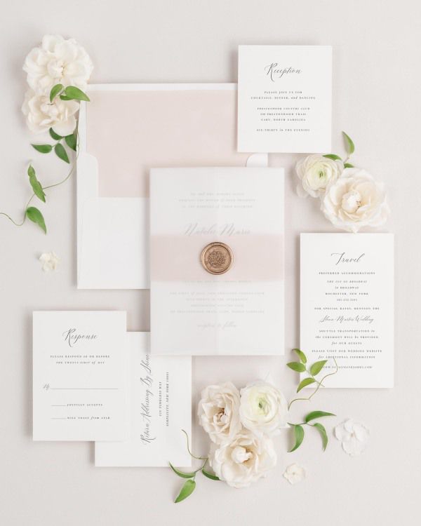 Natalie wedding invitations flat lay with rose gold solid liner, rose gold belly band, translucent vellum jacket, and gold florette wax seal.