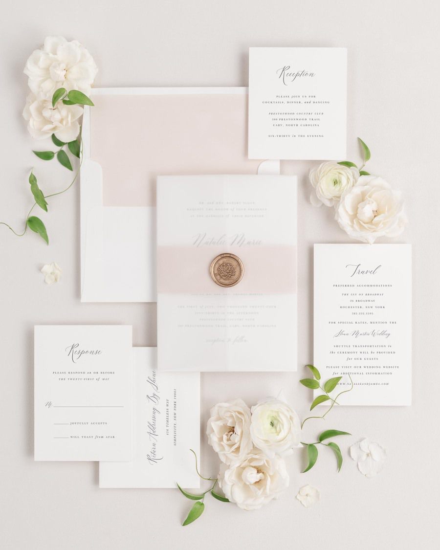 Natalie wedding invitations flat lay with rose gold solid liner, rose gold belly band, translucent vellum jacket, and gold florette wax seal.