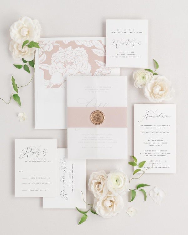 Ophelia wedding invitations flat lay with rosewater blooms liner, rosewater belly band, translucent vellum jacket, and gold florette wax seal.