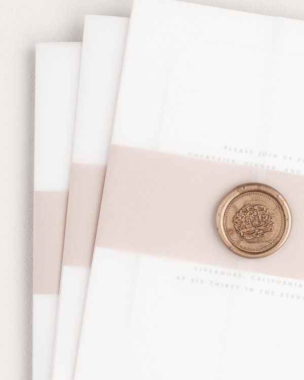 Ophelia wedding invitation with a rosewater belly band, translucent vellum jacket, and gold florette wax seal.