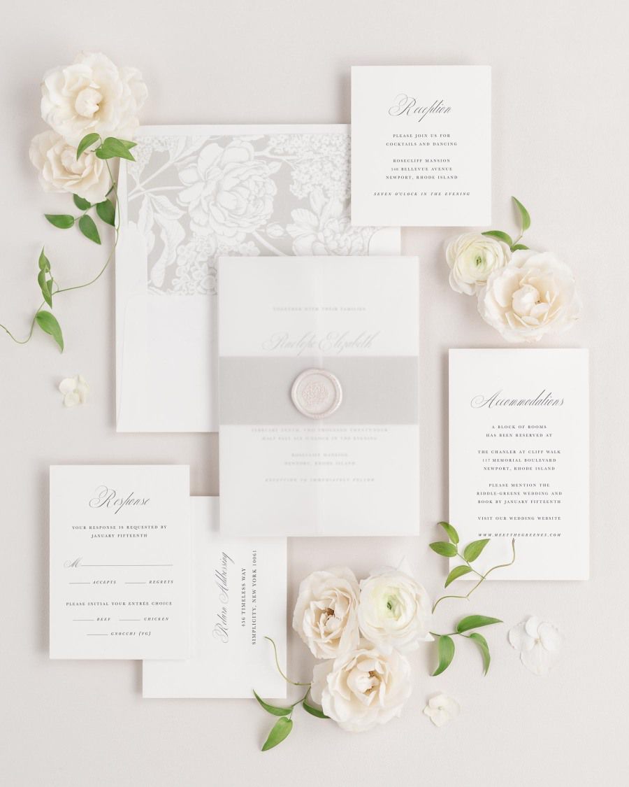 Penelope wedding invitations flat lay with stone belly band, translucent vellum jacket, and pearl florette wax seal.