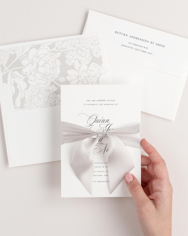 Bride holding Quinn wedding invitation tied with mink ribbon.
