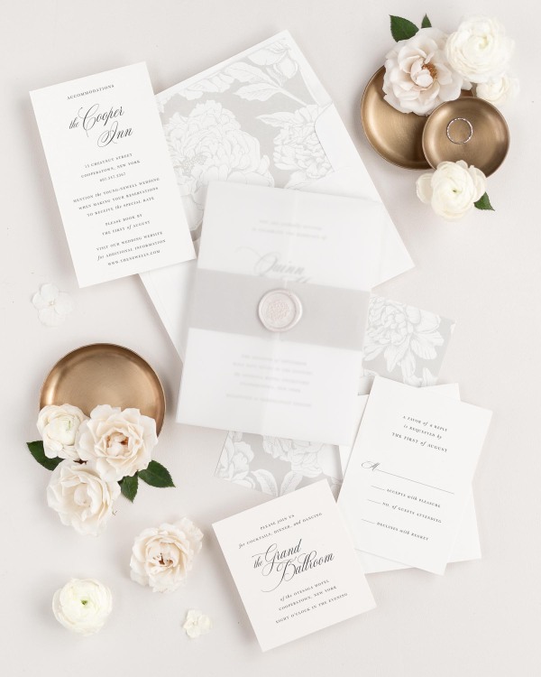 Quinn wedding invitations flat lay with stone blooms liner, stone belly band, translucent vellum jacket, and pearl posy wax seal.