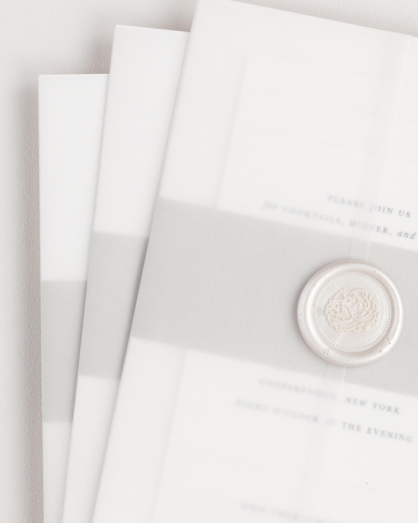 Quinn wedding invitation with a stone belly band, translucent vellum jacket, and pearl posy wax seal.