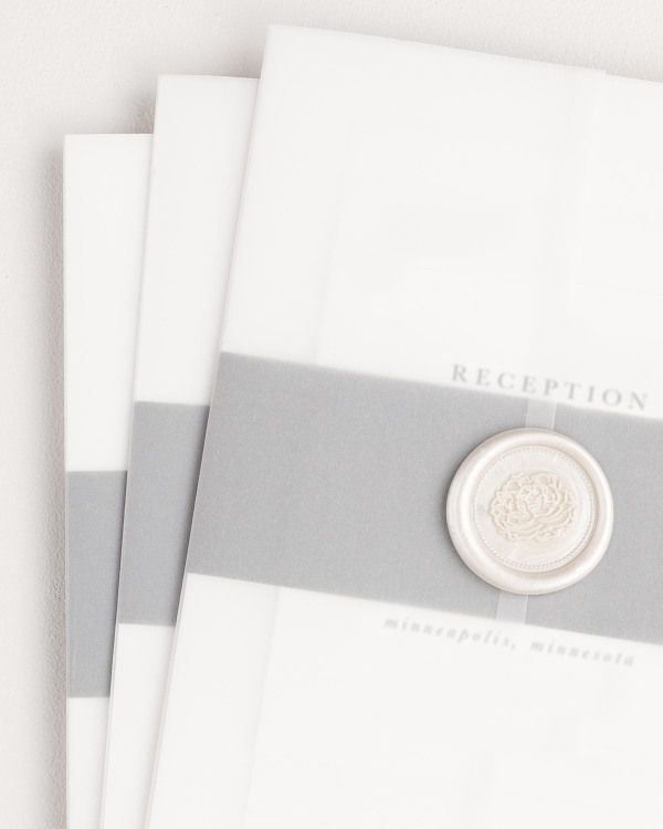 Reagan wedding invitation with a slate belly band, translucent vellum jacket, and pearl florette wax seal.