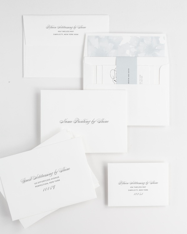 Script Elegance wedding invitation envelopes with guest addressing, return addressing, and name printing services. Inner envelope features a watercolor peonies liner and ice blue belly band.