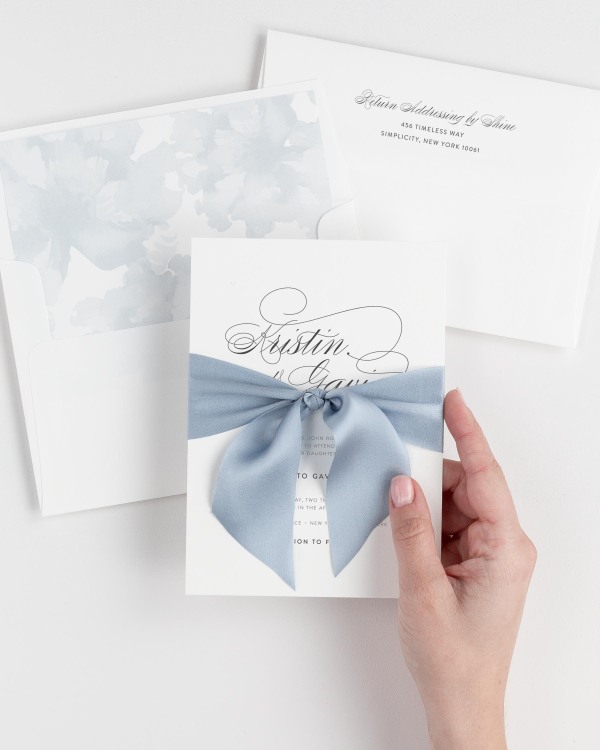Bride holding Script Elegance wedding invitation tied with french blue ribbon.