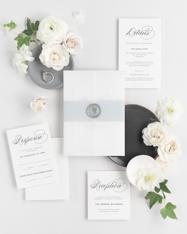 Script Elegance wedding invitations flat lay with ice blue belly band, translucent vellum jacket, and silver posy wax seal.