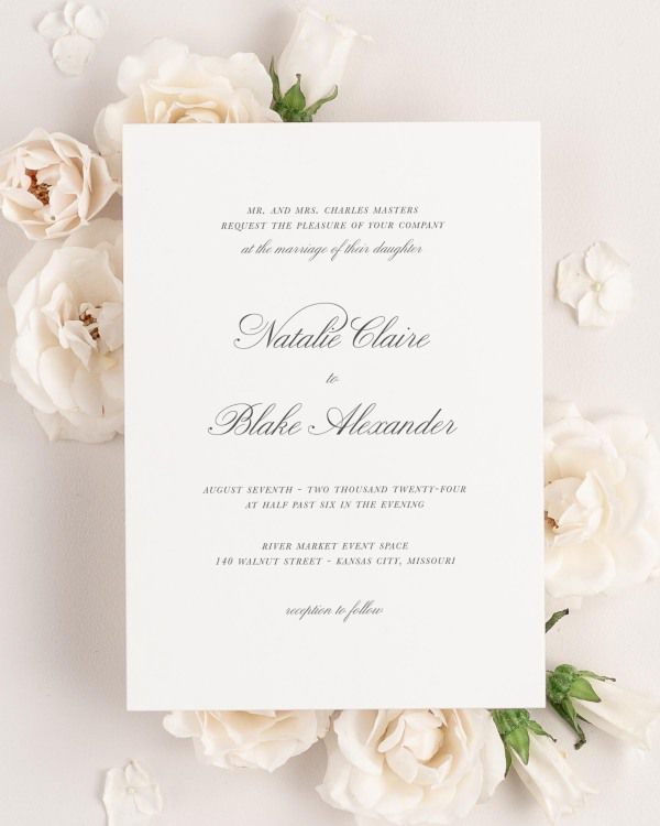 A Classic Script wedding invitation on a neutral background with simple flowers framing it. The invitation features a timeless font.