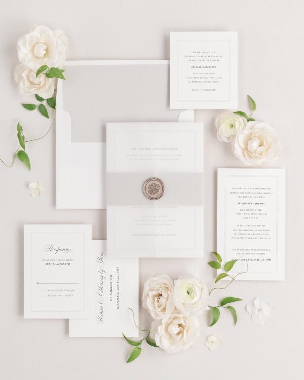 Simply Classic wedding invitations flat lay with stone belly band, translucent vellum jacket, and bronze florette wax seal.