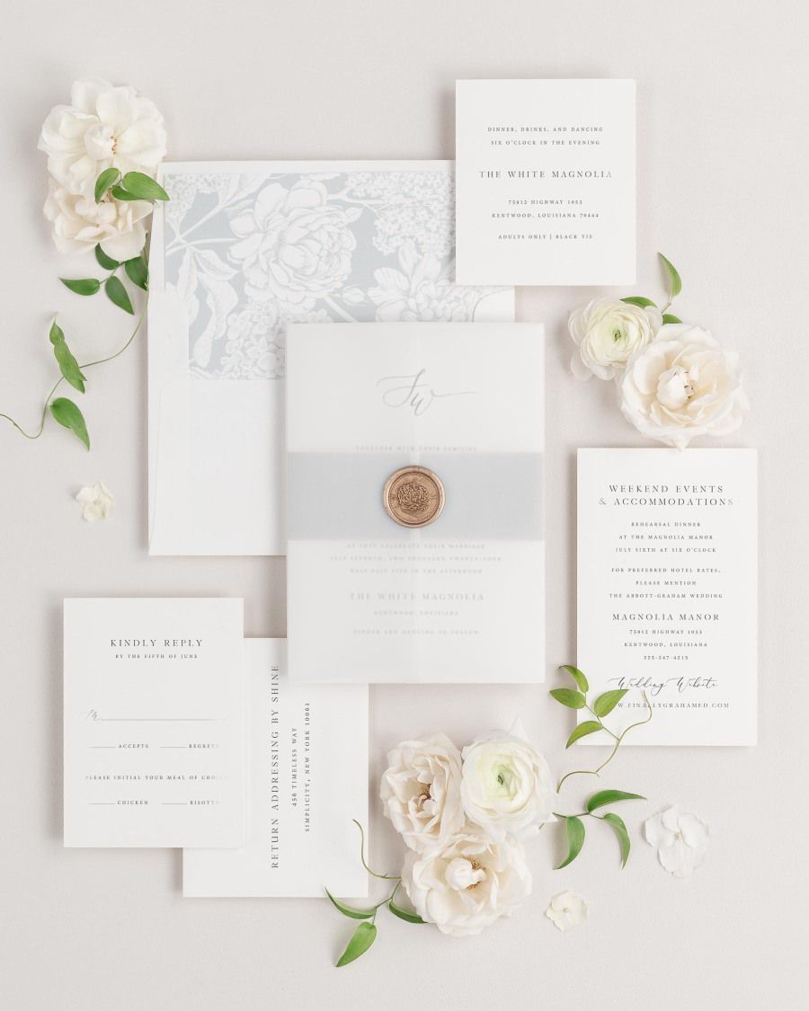 Sloan wedding invitations flat lay with cloud hydrangea liner, cloud belly band, translucent vellum jacket, and gold florette wax seal.