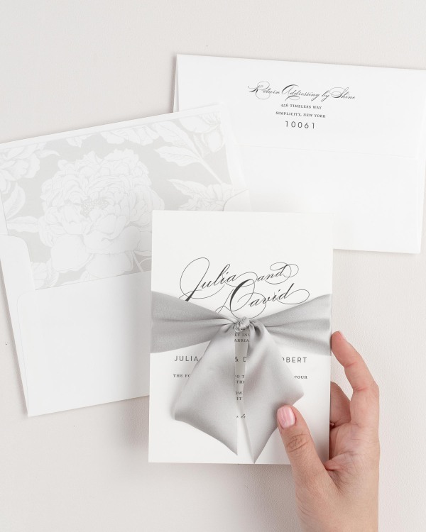 Bride holding Vintage Glam wedding invitation tied with fog ribbon.