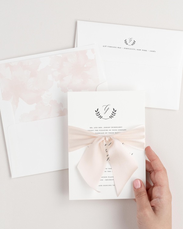 Bride holding Wreath Monogram wedding invitation tied with pale pink ribbon.
