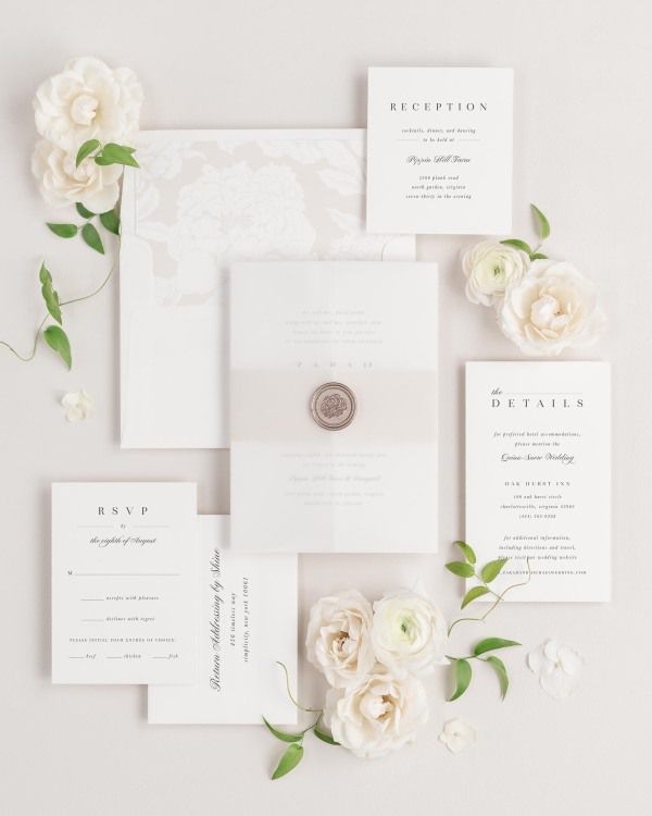 Zarah wedding invitations flat lay with nude blooms liner, nude belly band, translucent vellum jacket, and bronze florette wax seal.
