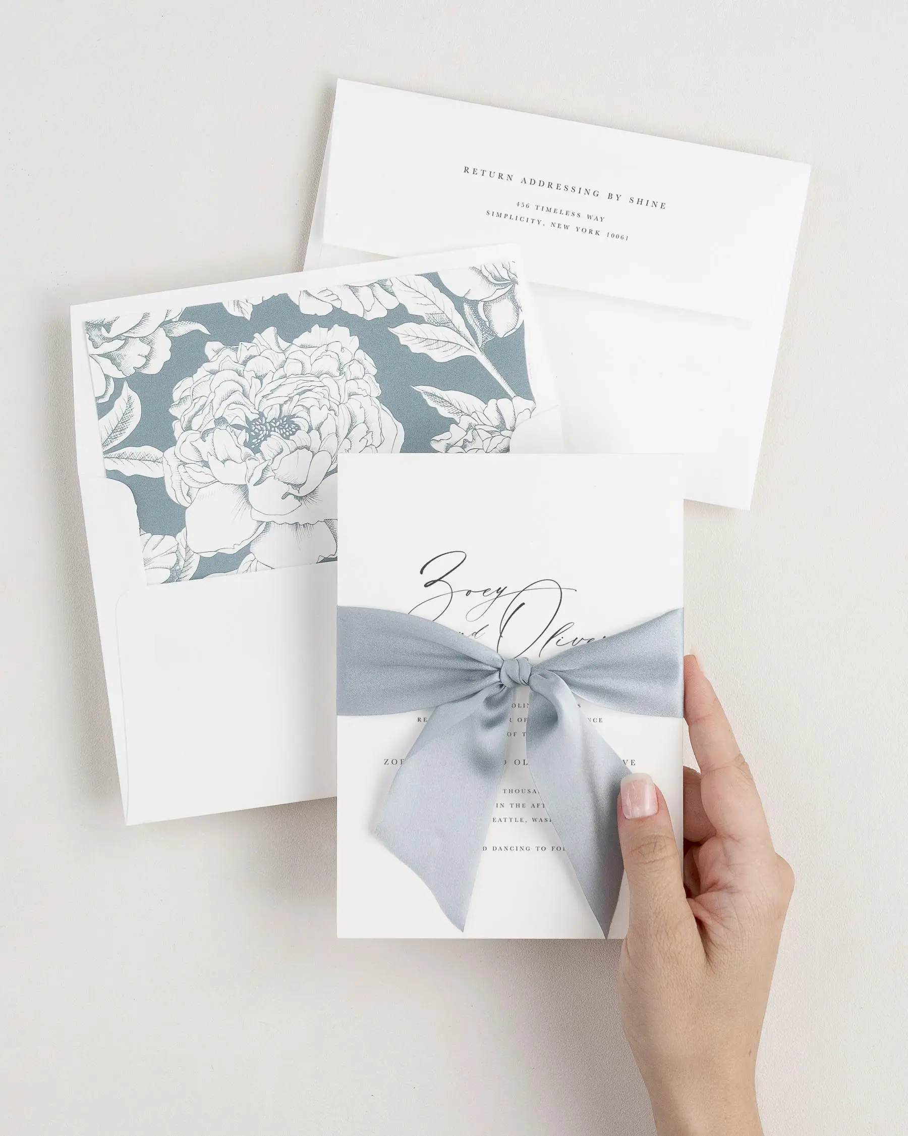 Bride holding Zoey wedding invitation tied with whisper blue ribbon.