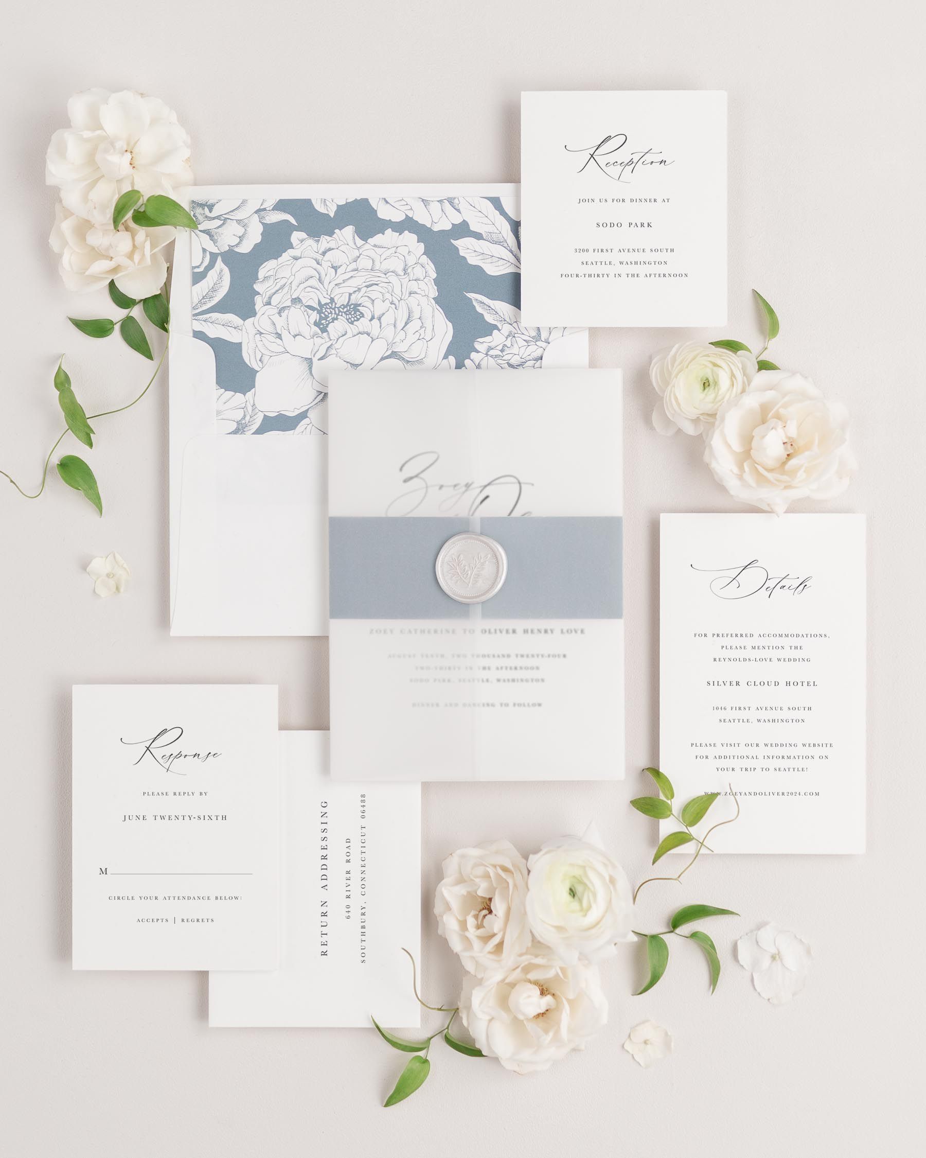 Zoey wedding invitations flat lay with mineral blooms liner, mineral belly band, translucent vellum jacket, and pearl wreath wax seal.