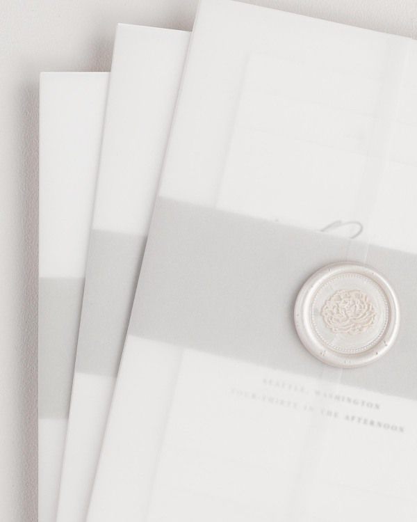 Zoey wedding invitation with a stone belly band, translucent vellum jacket, and pearl florette wax seal.