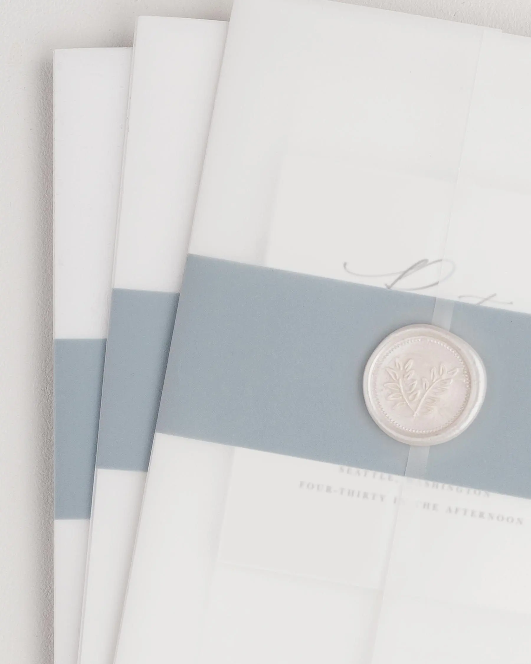 Zoey wedding invitation with a mineral belly band, translucent vellum jacket, and pearl wreath wax seal.